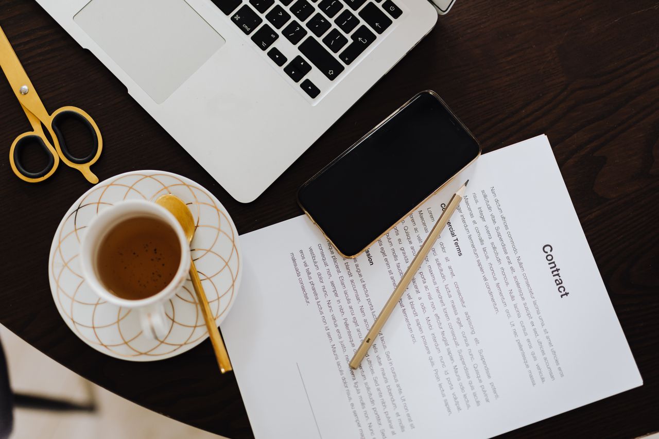Over ons Top-view of a workspace with contract, coffee, laptop, and smartphone focused on business productivity.